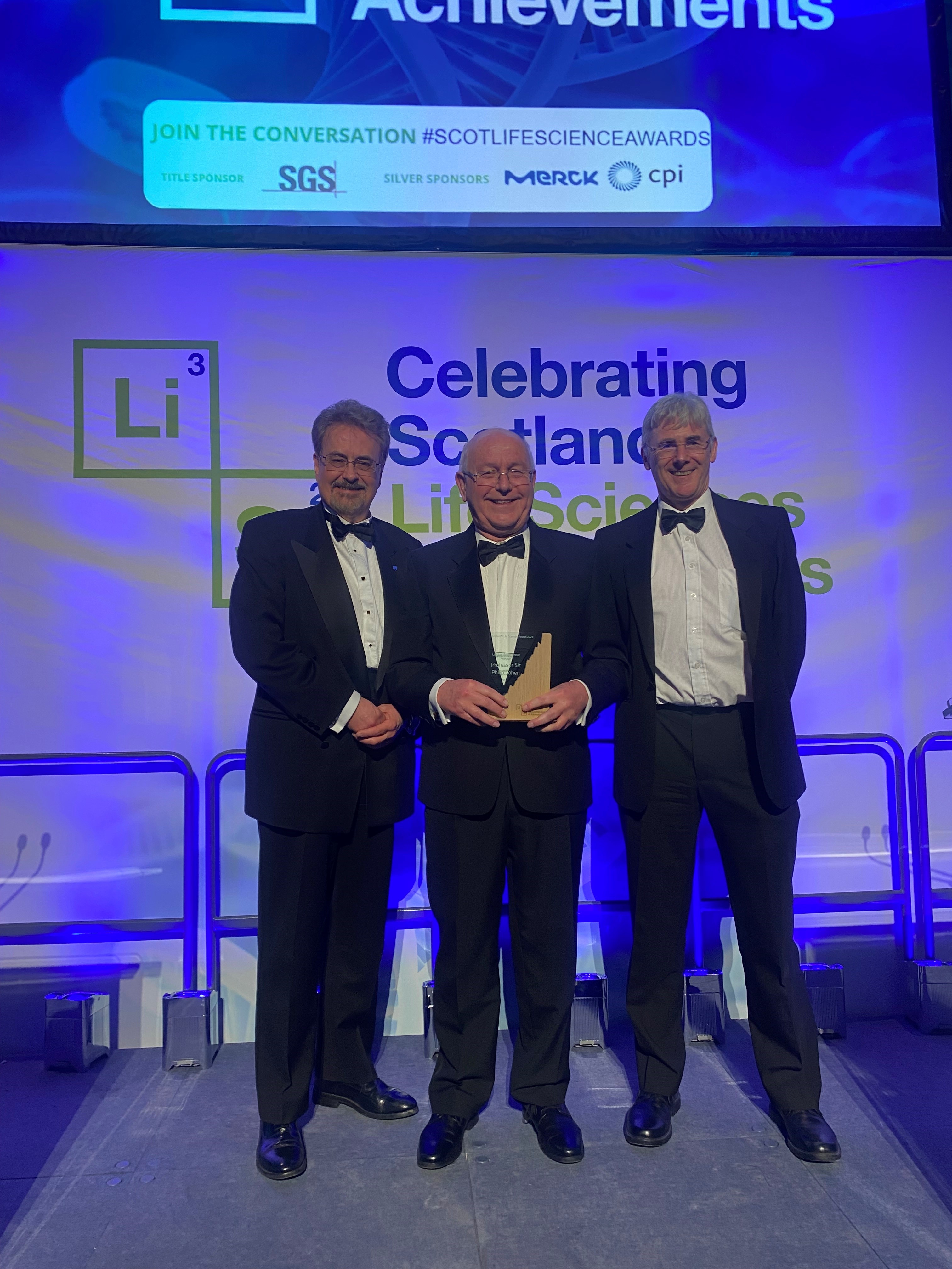 Philip Cohen holding the Lifetime Achievement Award, with Ian Gillespie, Principal and Vice Chancellor of the University of Dundee (Left) and Julian Blow, Dean of Life Science at the University of Dundee (right)